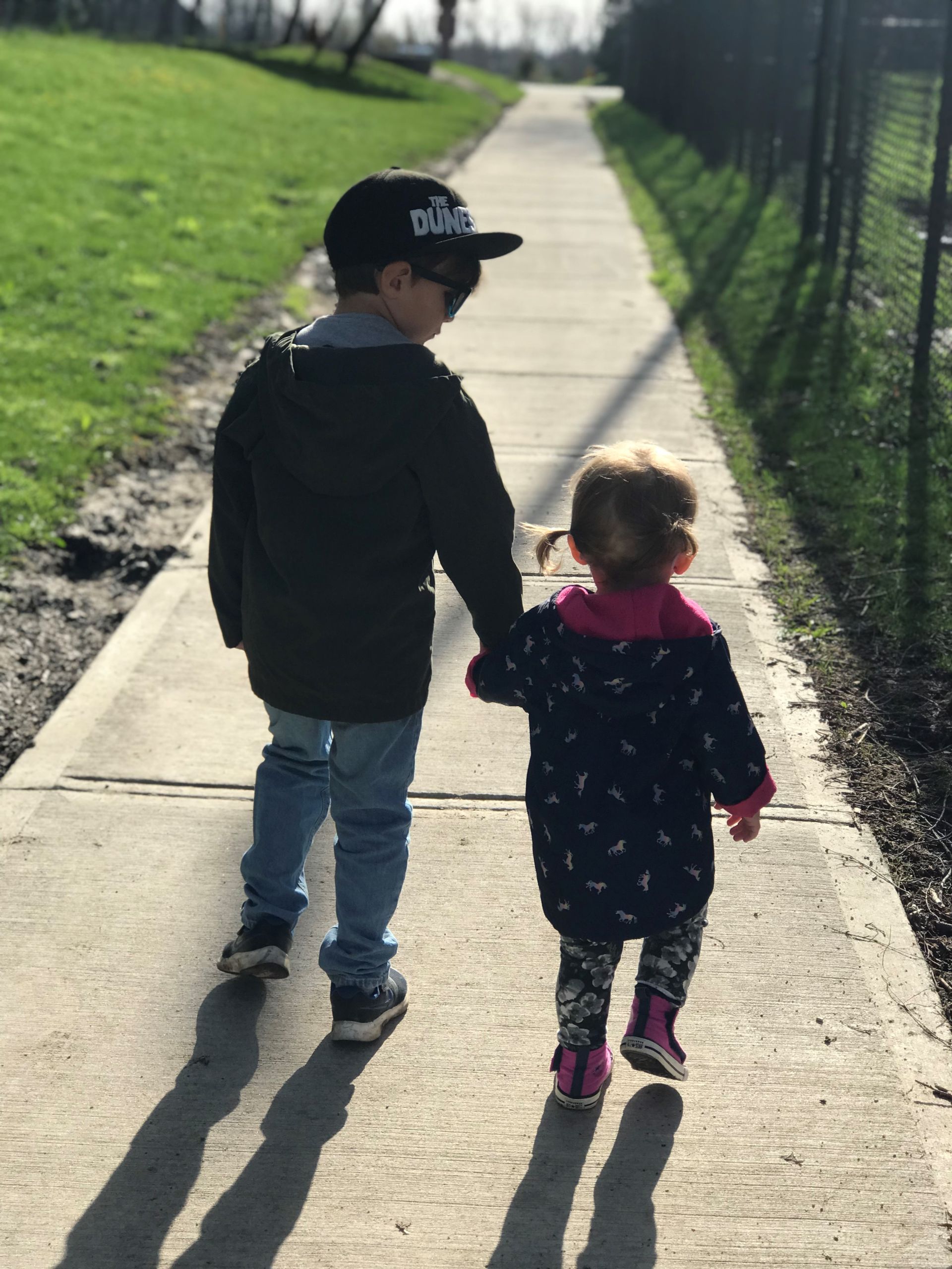 A photo showing a little boy and girl walking on a sidewalk holding hands.
